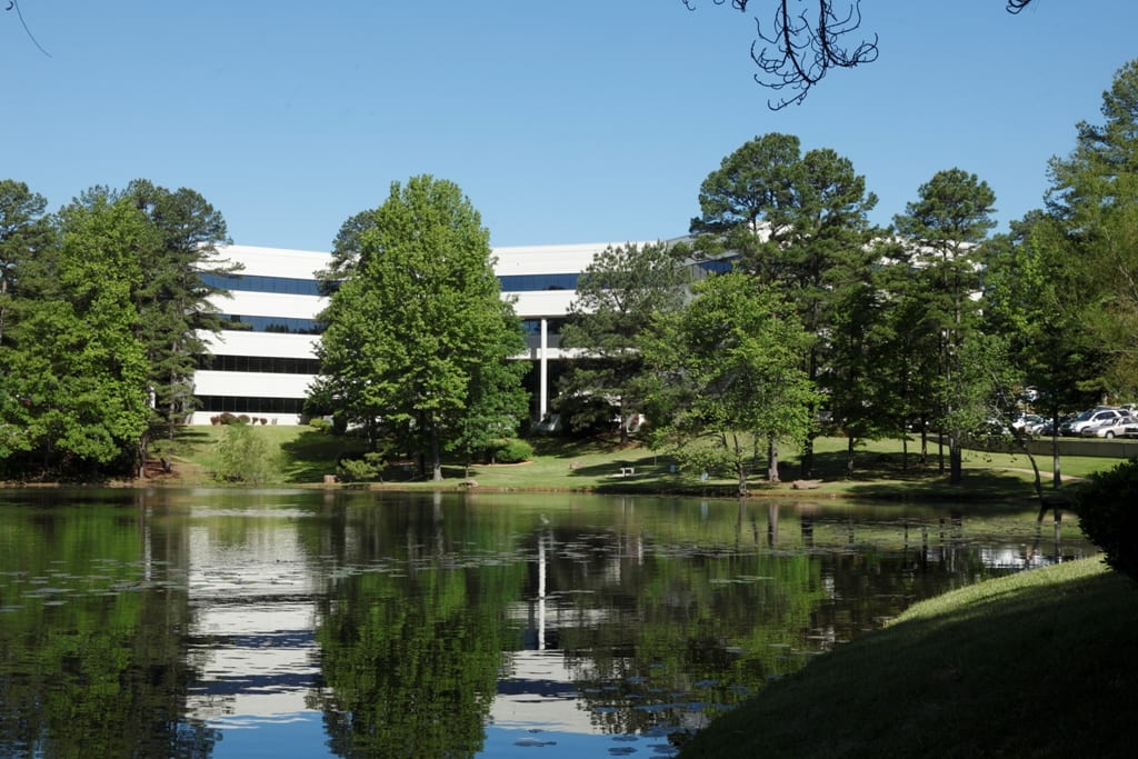 A white building with long windows surrounded by lots of trees and a lake
