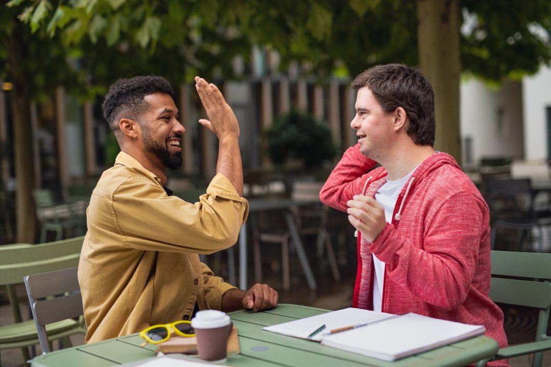 Two men sit at a table and give each other a high five.